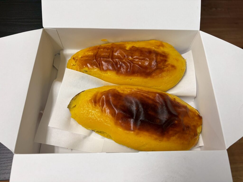 Two yellow-orange baked pastries in a white takeout box resting on a paper napkin.