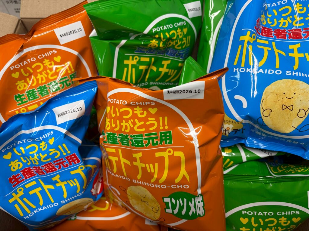 Pile of colorful potato chips bags (orange, blue, green) with bold Japanese text on each package.
